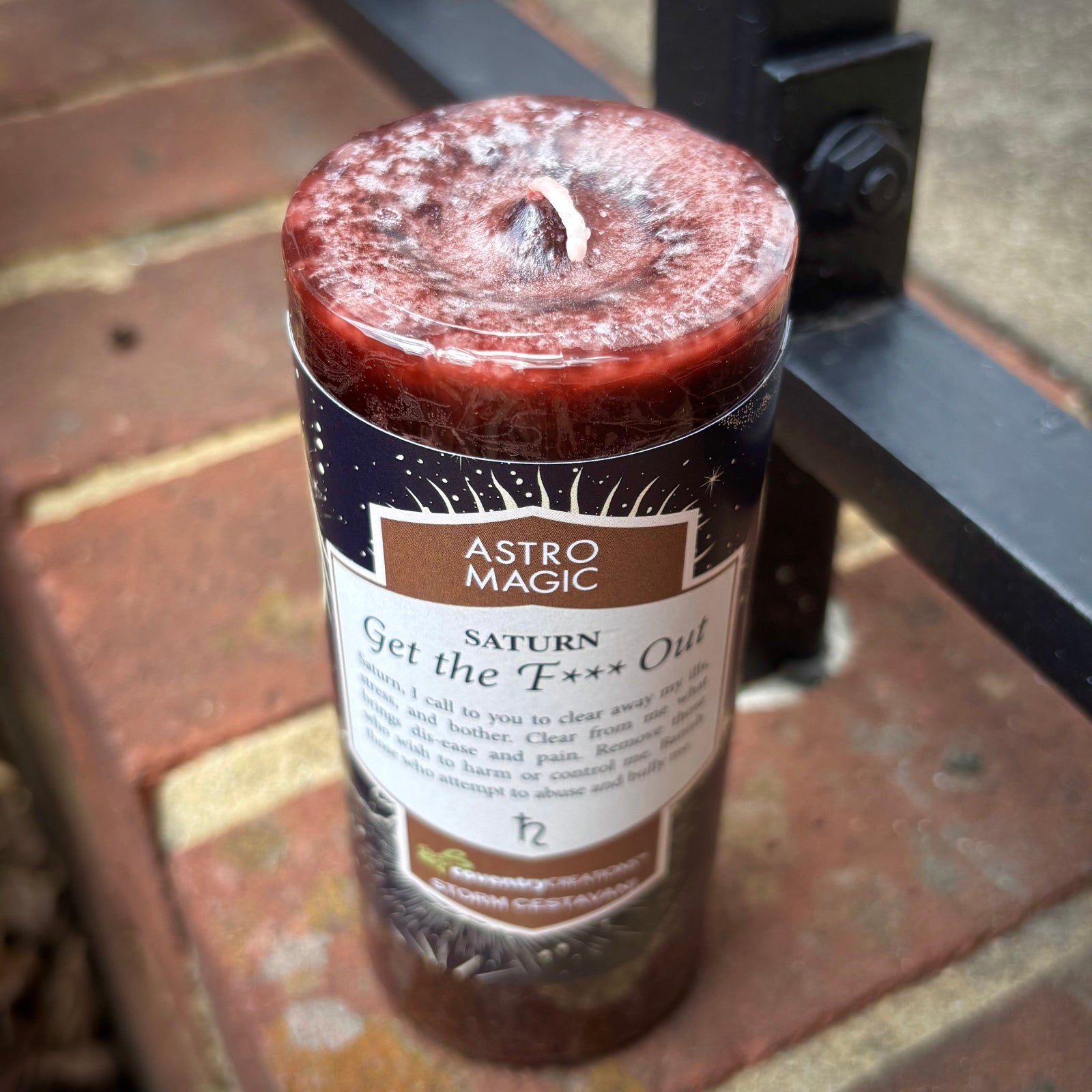 The Astro Magic Saturn - Get the F* Out Candle sitting on a brick.