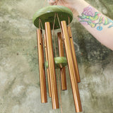 An up-close image of someone holding the Green Dragonfly Woodstock Habitats™ Wind Chime in front of a concrete wall.