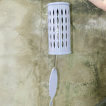 An up-close image of someone holding the Lavender Mist Bamboo Aloha Wind Chime in front of a concrete wall.
