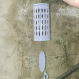 Someone holding the Lavender Mist Bamboo Aloha Wind Chime in front of a concrete wall.