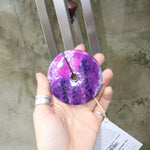 An up-close image of someone holding the Woodstock Amethyst Wind Chime in front of a concrete wall.