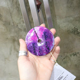 An up-close image of someone holding the Woodstock Amethyst Wind Chime in front of a concrete wall.