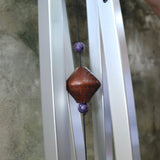 An up-close image of someone holding the Woodstock Amethyst Wind Chime in front of a concrete wall.