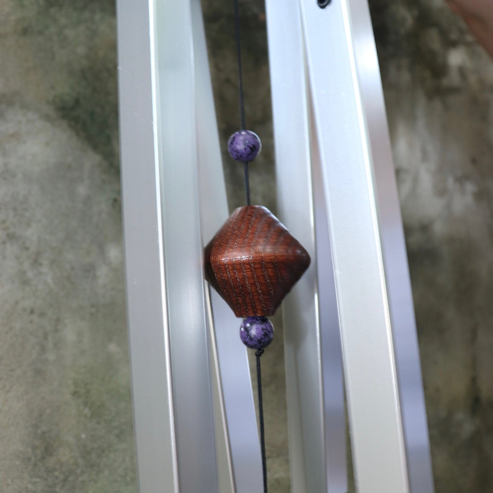 An up-close image of someone holding the Woodstock Amethyst Wind Chime in front of a concrete wall.