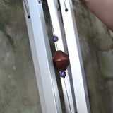 An up-close image of someone holding the Woodstock Amethyst Wind Chime in front of a concrete wall.