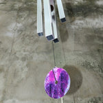 An up-close image of someone holding the Woodstock Amethyst Wind Chime in front of a concrete wall.