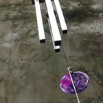 An up-close image of someone holding the Woodstock Amethyst Wind Chime in front of a concrete wall.