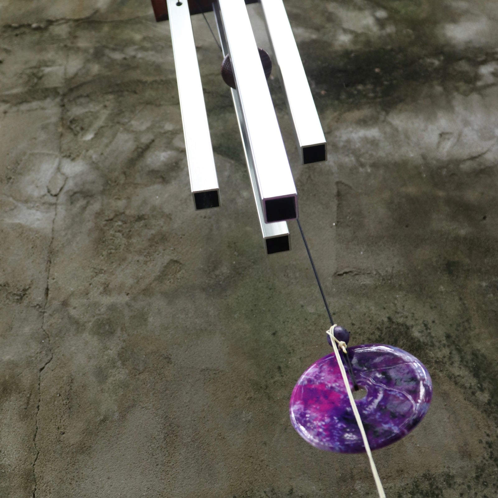 An up-close image of someone holding the Woodstock Amethyst Wind Chime in front of a concrete wall.