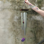 Someone holding the Woodstock Amethyst Wind Chime in front of a concrete wall.