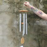 Someone holding the Woodstock Reflections Wind Chime in front of a concrete wall.