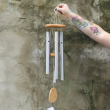 Someone holding the Woodstock Reflections Wind Chime in front of a concrete wall.