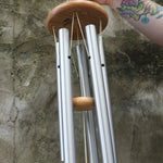 An up-close image of someone holding the Woodstock Reflections Wind Chime in front of a concrete wall.