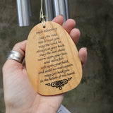 An up-close image of someone holding the wood burned Irish Blessing piece of the wind chime in front of a concrete wall.