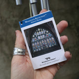 An up-close image of someone holding the Serenity Prayer Woodstock Reflections Wind Chime in front of a concrete wall.