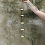Someone holding the Brass Quintet Woodstock Temple Bells Wind Chime in front of a concrete wall.