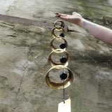 An up-close image of someone holding the Brass Quintet Woodstock Temple Bells Wind Chime in front of a concrete wall.