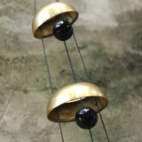 An up-close image of someone holding the Brass Quintet Woodstock Temple Bells Wind Chime in front of a concrete wall.