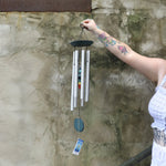 Someone holding up the Seven Stone Blue Woodstock Chakra Chime in front of a concrete wall.