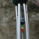 An up-close image of someone holding up the Seven Stone Blue Woodstock Chakra Chime in front of a concrete wall.