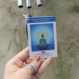 An up-close image of someone holding up the tag of the Seven Stone Blue Woodstock Chakra Chime in front of a concrete wall.