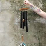 Someone holding the Black Woodstock Craftsman Chime in front of a concrete wall.