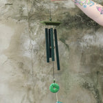 Someone holding the Woodstock Jade Wind Chime in front of a concrete wall.