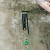 Someone holding the Woodstock Jade Wind Chime in front of a concrete wall.