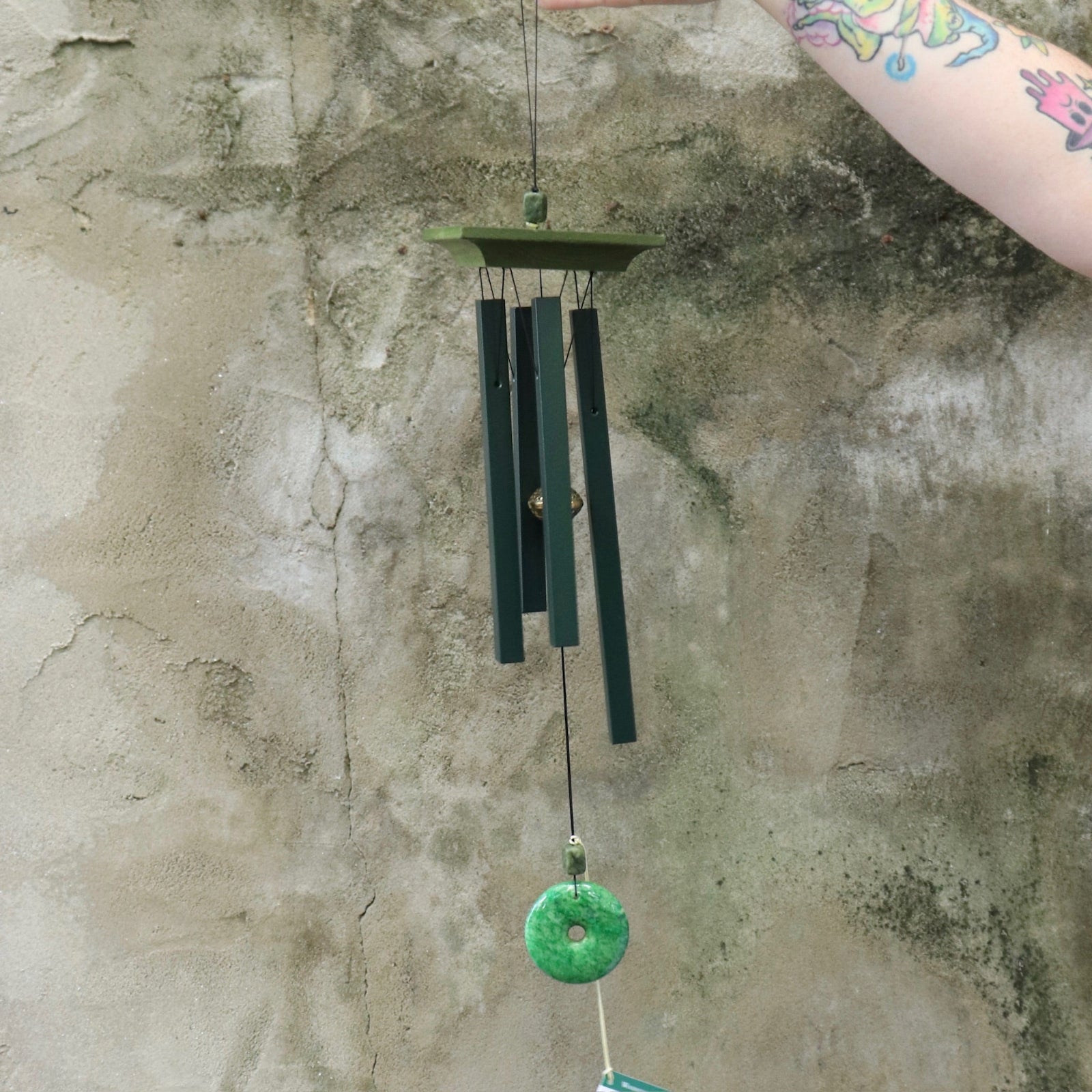 Someone holding the Woodstock Jade Wind Chime in front of a concrete wall.