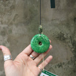 An up-close image of someone holding the Woodstock Jade Wind Chime in front of a concrete wall.