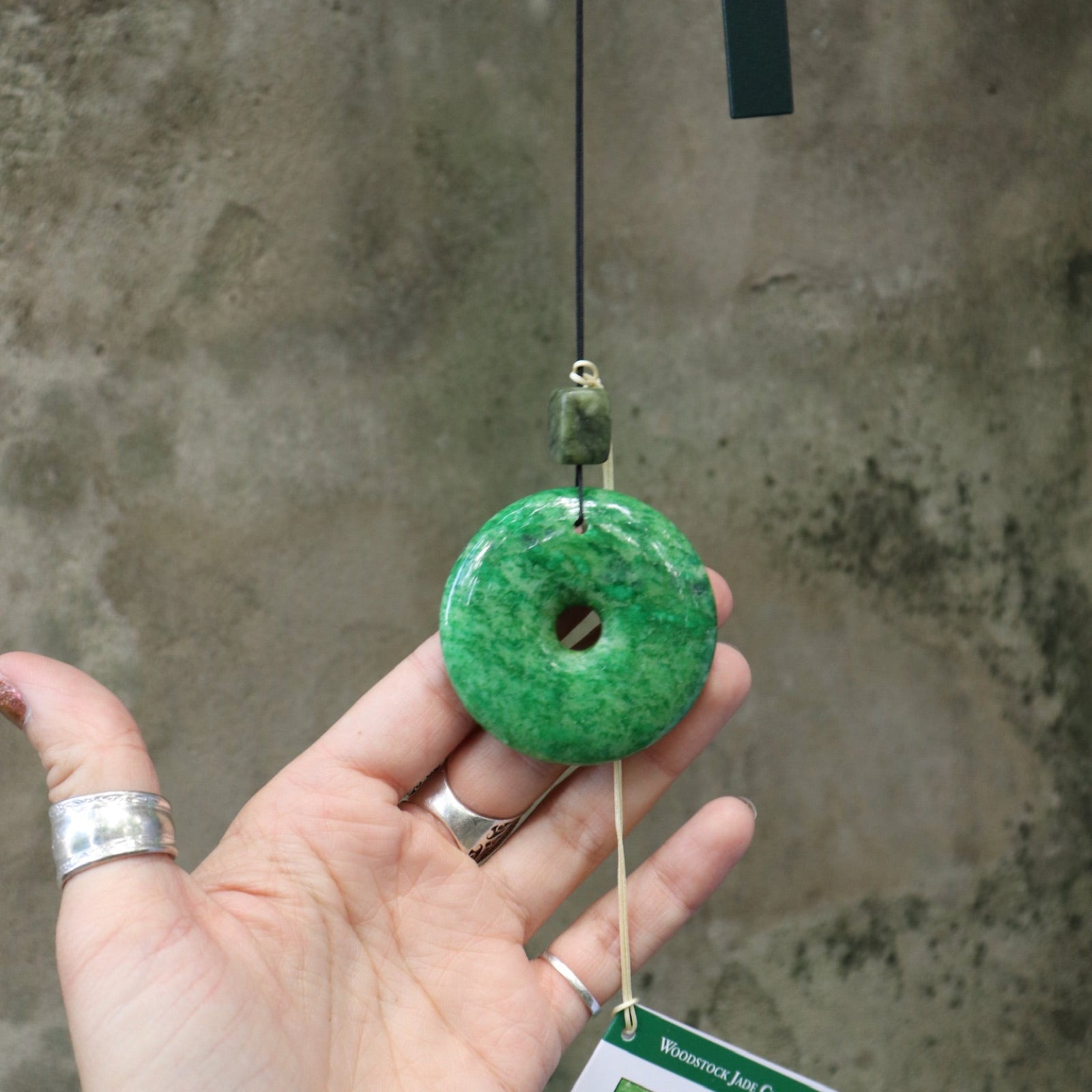 An up-close image of someone holding the Woodstock Jade Wind Chime in front of a concrete wall.