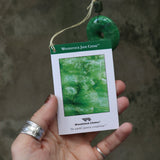 An up-close image of someone holding the tag of the Woodstock Jade Wind Chime in front of a concrete wall.