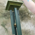 An up-close image of someone holding the Evergreen Woodstock Jade Wind Chime in front of a concrete wall.