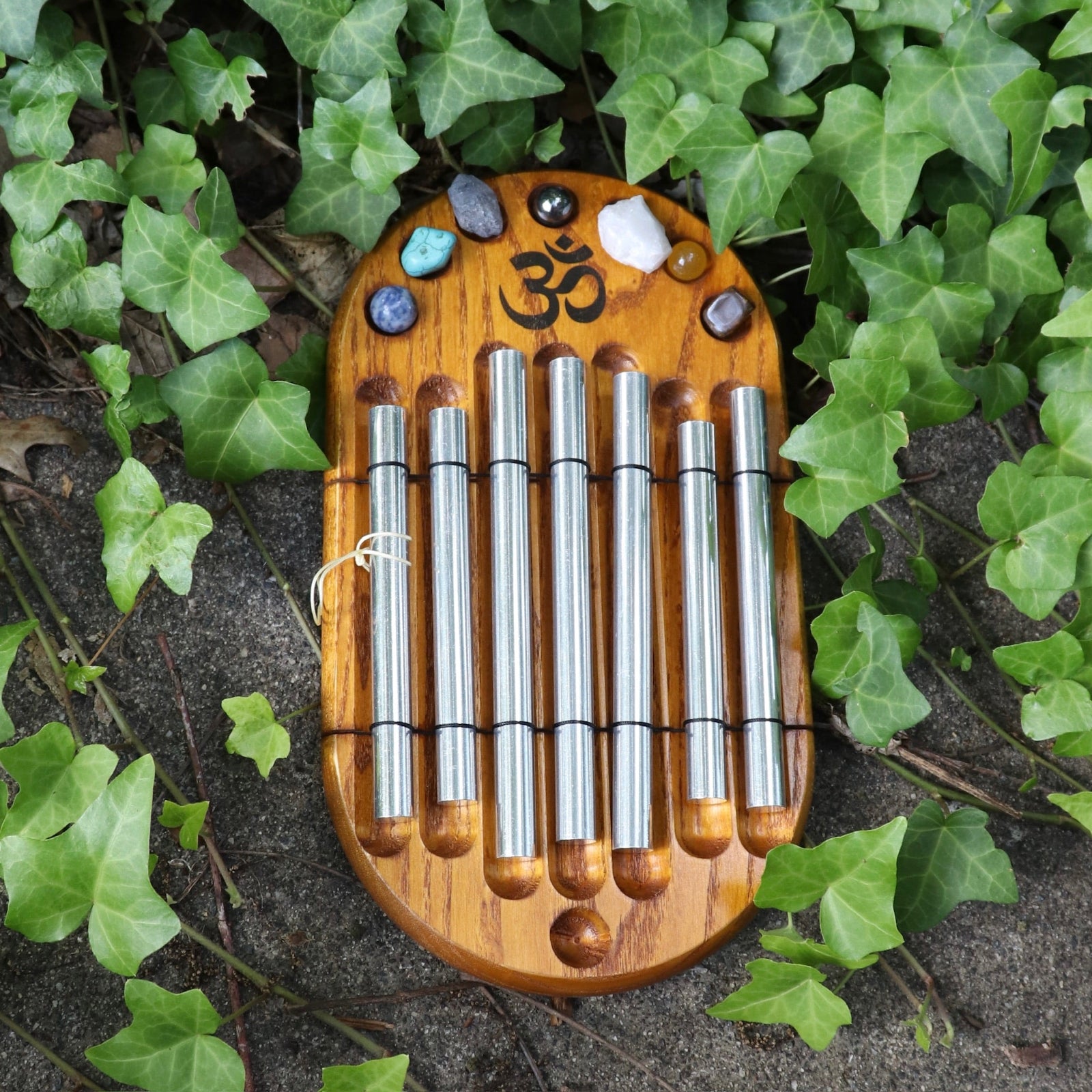 The Woodstock Zenergy Chakra Chime on a cement background with ivy surrounding it.