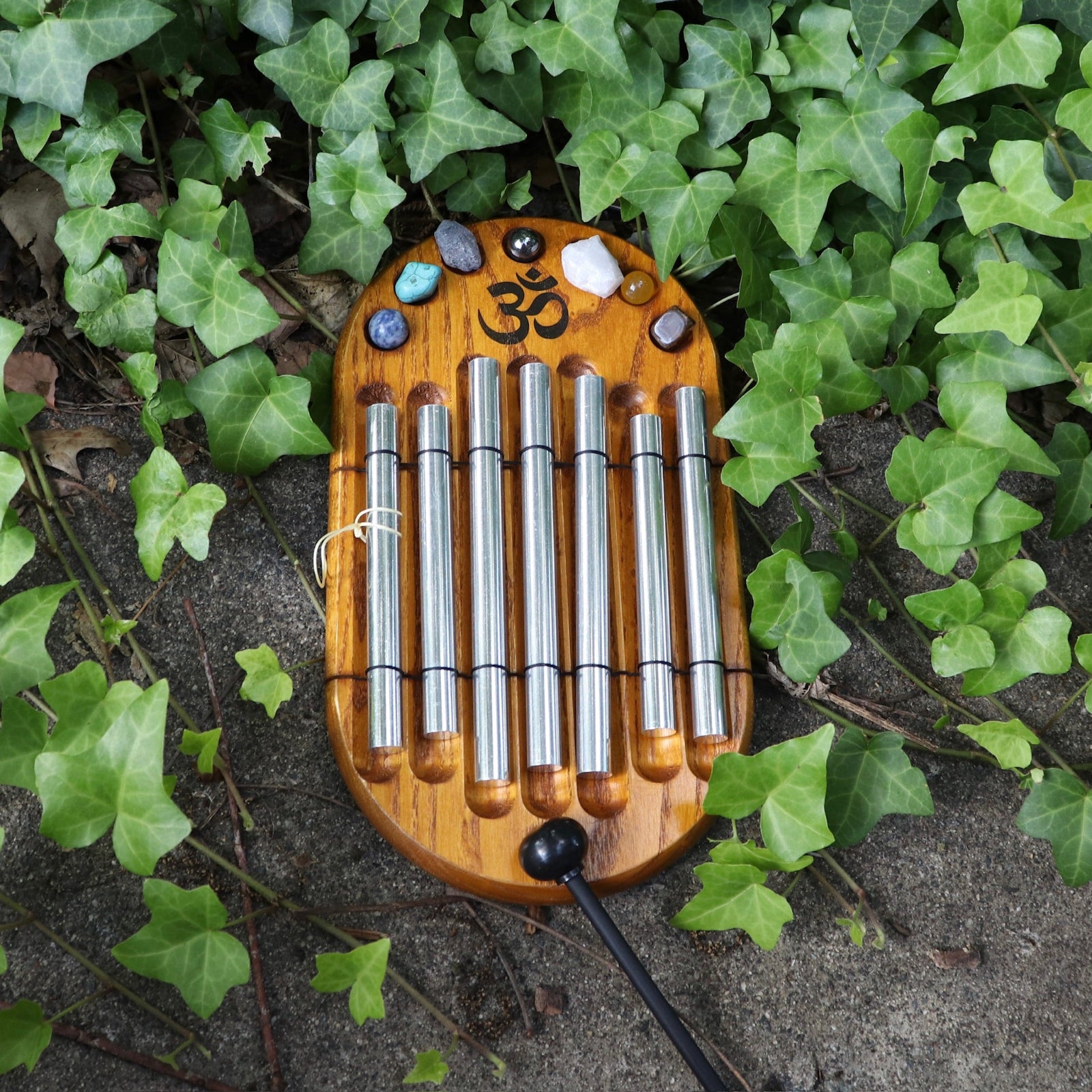 The Woodstock Zenergy Chakra Chime on a cement background with ivy surrounding it.