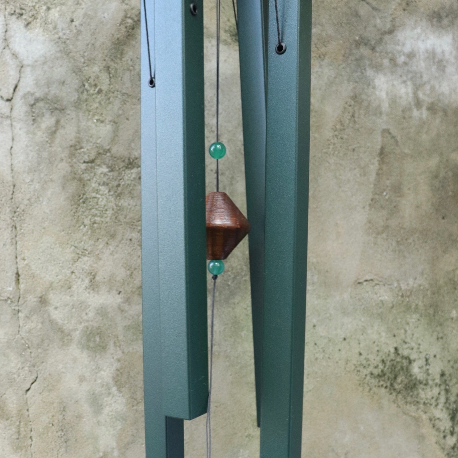 An up-close image of someone holding the Evergreen Woodstock Craftsman Wind Chime in front of a concrete wall.
