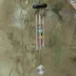 Someone holding the Seven Stones Silver Woodstock Chakra Chime in front of a concrete wall.