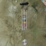 Someone holding the Seven Stones Silver Woodstock Chakra Chime in front of a concrete wall.