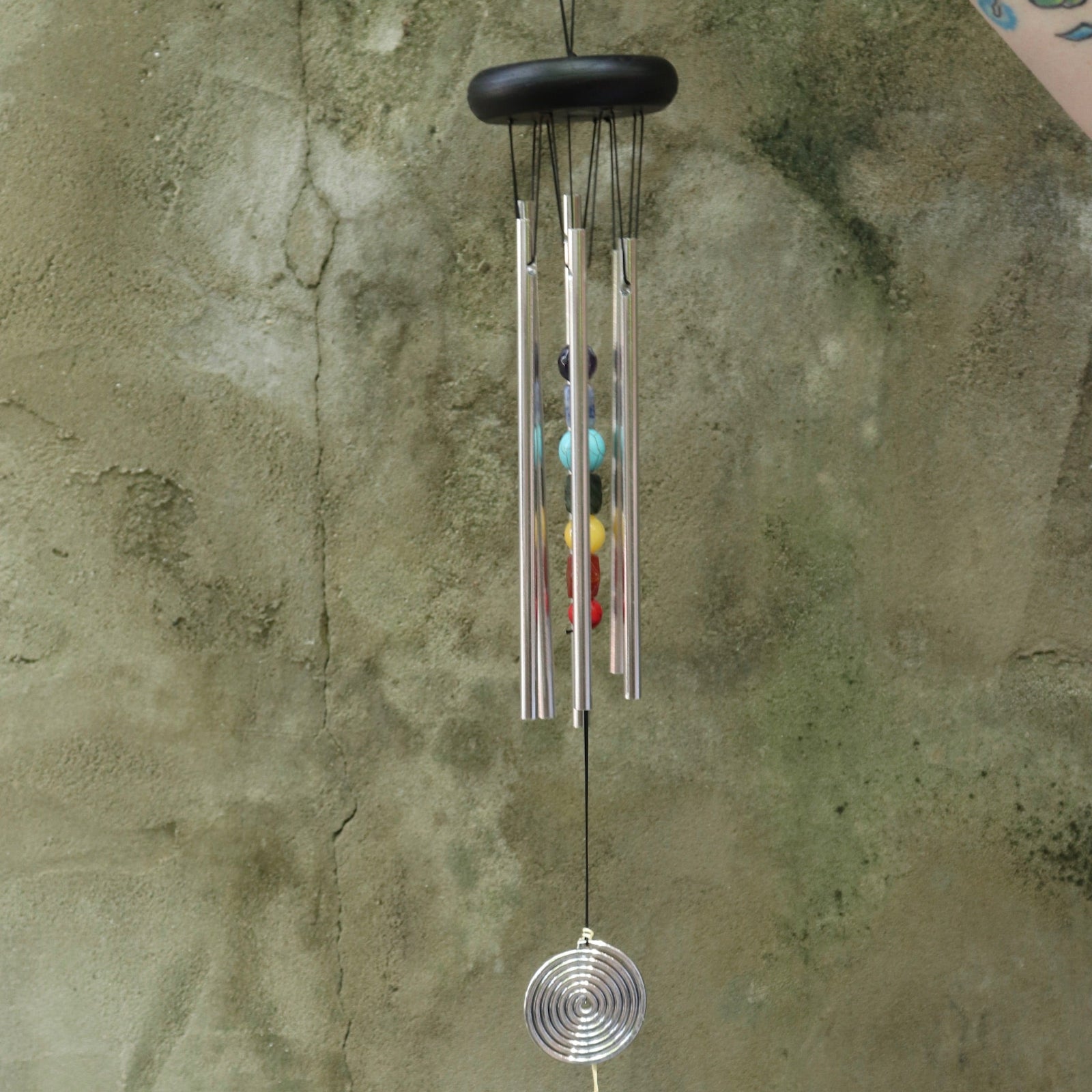 Someone holding the Seven Stones Silver Woodstock Chakra Chime in front of a concrete wall.