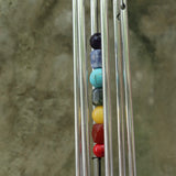 An up-close image of someone holding the Seven Stones Silver Woodstock Chakra Chime in front of a concrete wall.