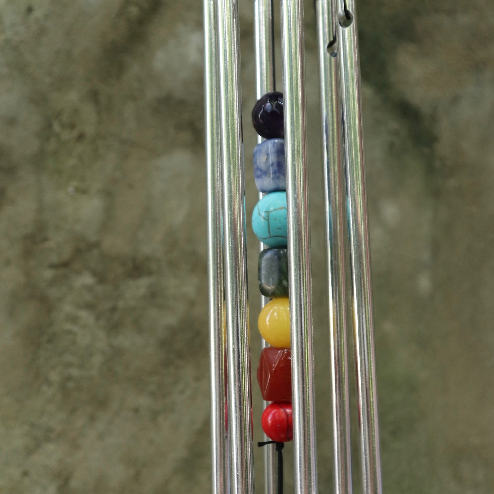 An up-close image of someone holding the Seven Stones Silver Woodstock Chakra Chime in front of a concrete wall.