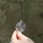 An up-close image of someone holding the Seven Stones Silver Woodstock Chakra Chime in front of a concrete wall.