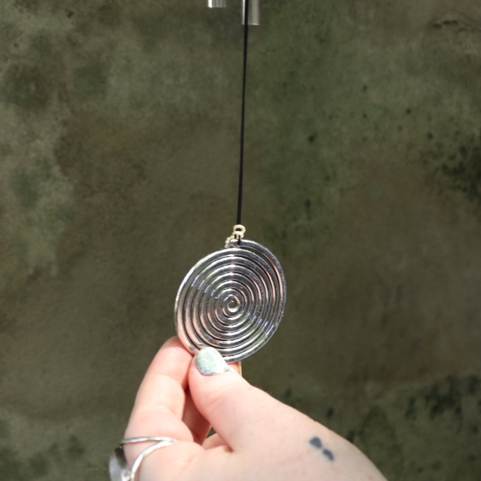 An up-close image of someone holding the Seven Stones Silver Woodstock Chakra Chime in front of a concrete wall.