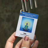 An up-close image of someone holding the tag of the Seven Stones Silver Woodstock Chakra Chime in front of a concrete wall.
