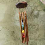 Someone holding the Seven Stones Bronze Woodstock Chakra Chime in front of a concrete wall.