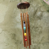 Someone holding the Seven Stones Bronze Woodstock Chakra Chime in front of a concrete wall.