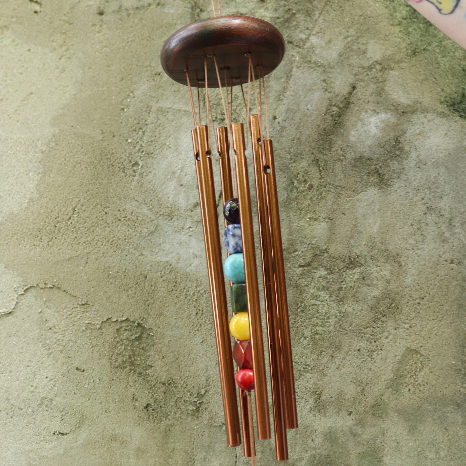 Someone holding the Seven Stones Bronze Woodstock Chakra Chime in front of a concrete wall.