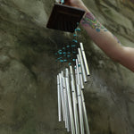 Someone holding the Turquoise Mystic Spiral Woodstock Wind Chime in front of a concrete wall.