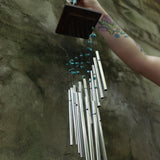 Someone holding the Turquoise Mystic Spiral Woodstock Wind Chime in front of a concrete wall.