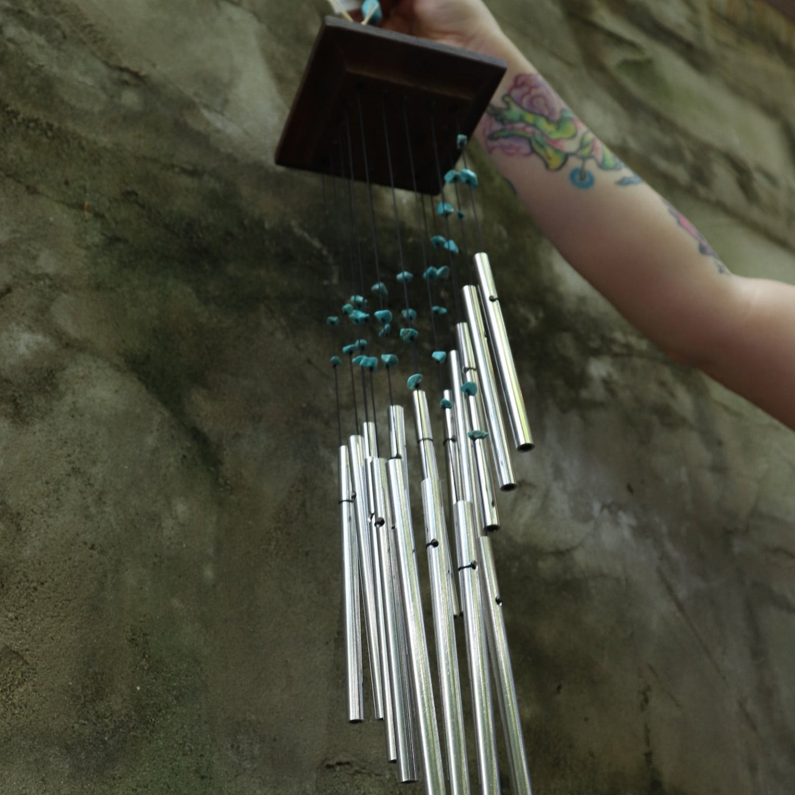 Someone holding the Turquoise Mystic Spiral Woodstock Wind Chime in front of a concrete wall.