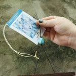 An up-close image of someone holding the tag of the Turquoise Mystic Spiral Woodstock Wind Chime in front of a concrete wall.